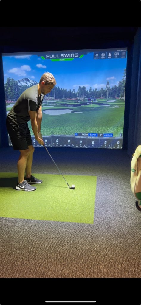 Golfer putting on the hitting mat in a One Swing Away simulator bay