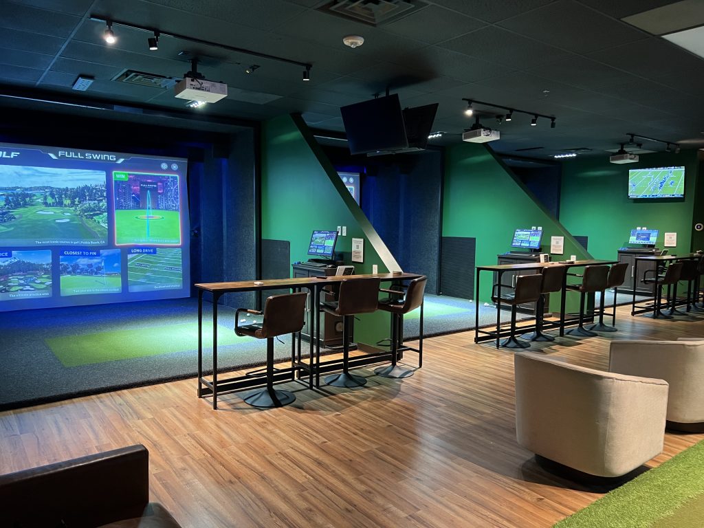 Wide view of the indoor golf bays and seating at One Swing Away